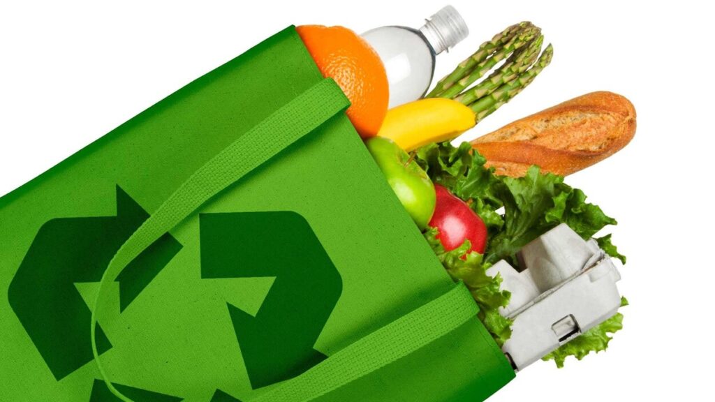 Sac d'épicerie vert avec enseigne recyclable. À l'intérieur du sac se trouvent des fruits et des légumes sans emballage de plastique.